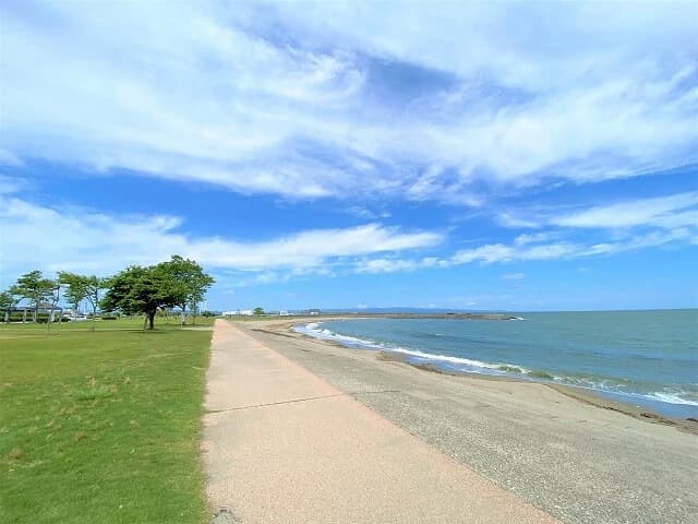 晴れた日の海老江海浜公園。芝生広場と海沿いの遊歩道、砂浜と波打ち際が続いている