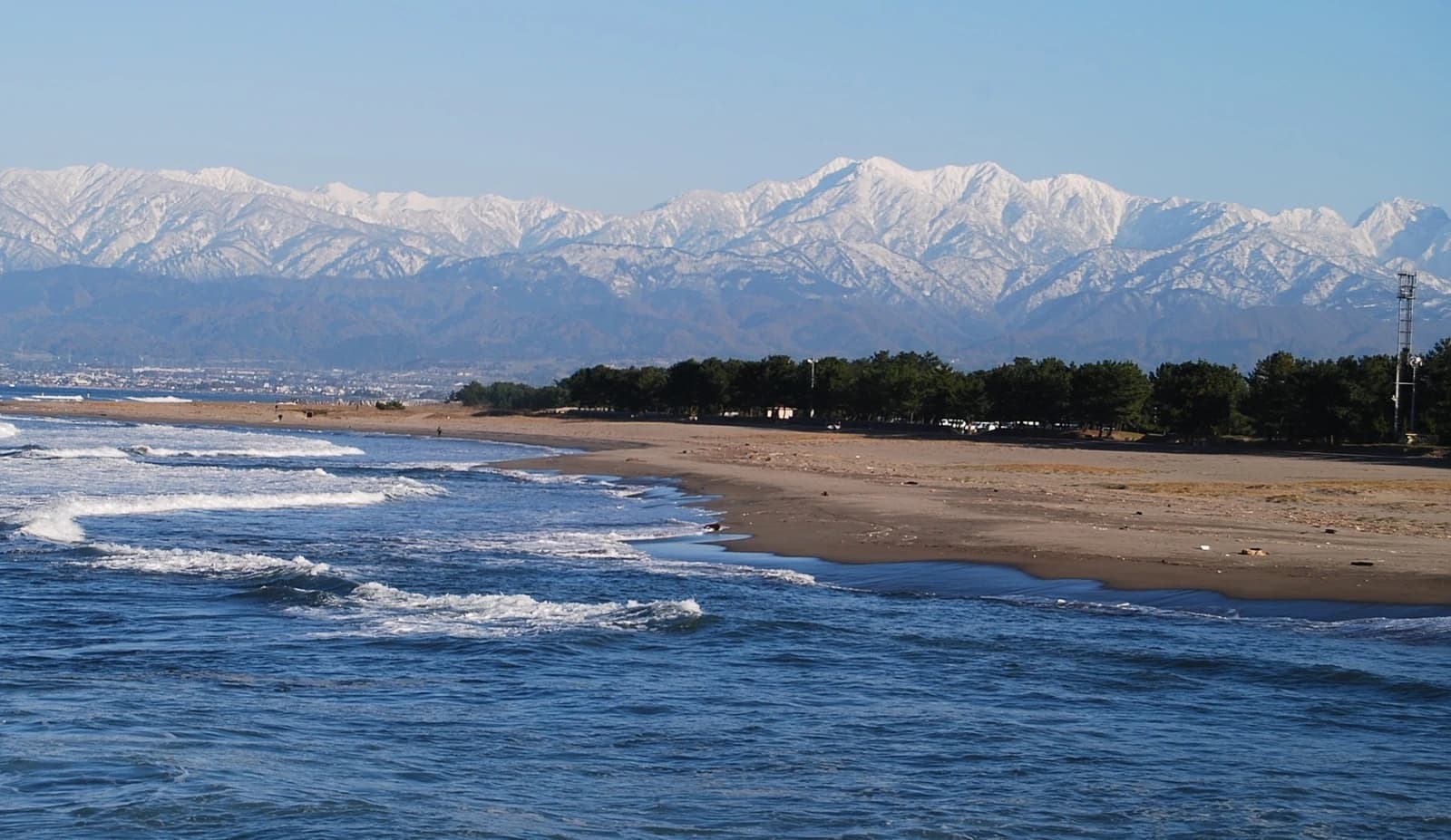岩瀬浜。波が寄せる広い砂浜と松林の向こうに、雪をかぶった立山連峰が見える